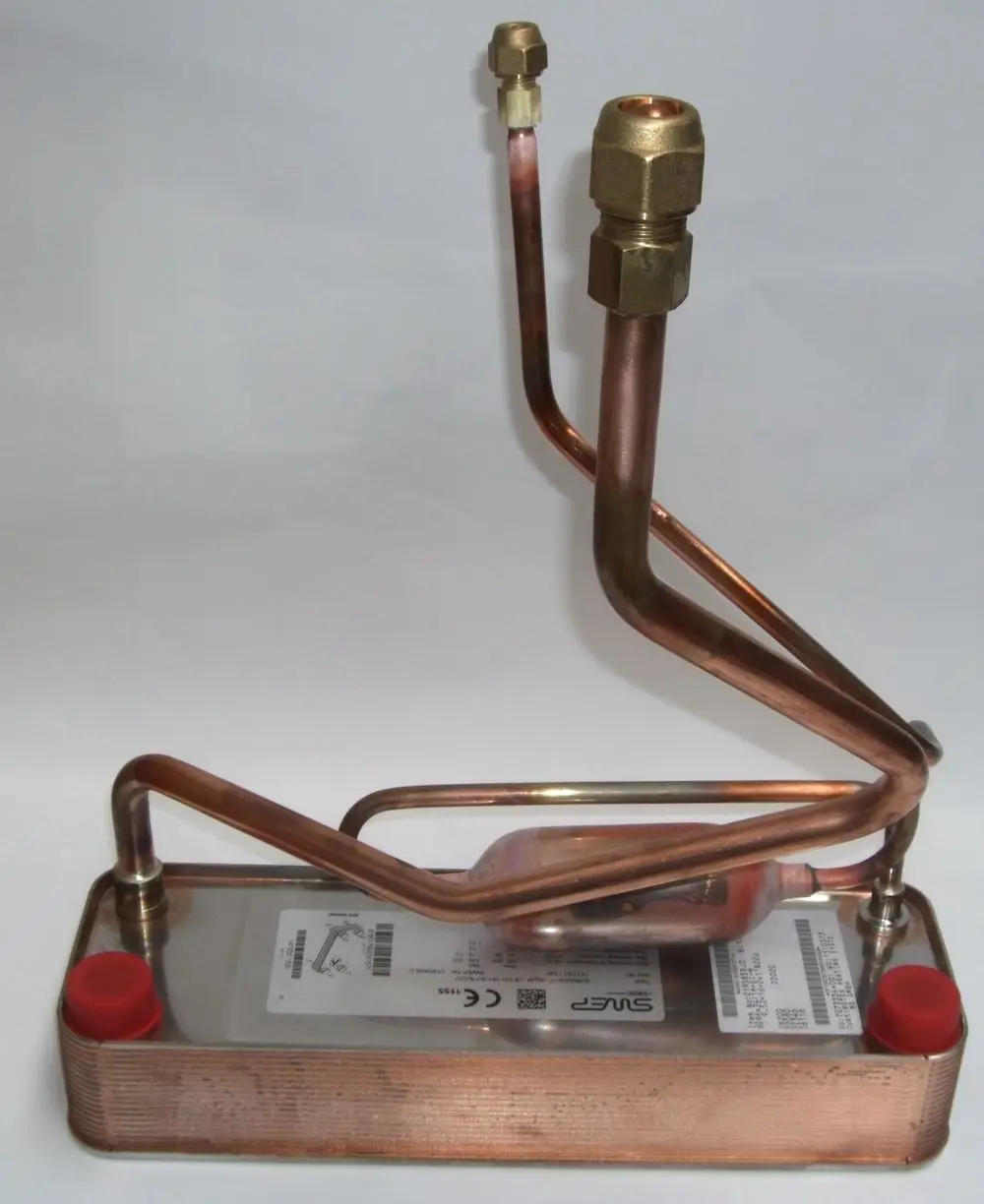 Kupferner Plattenwärmetauscher mit mehreren Rohrleitungen und Anschlüssen. Hersteller Daikin. Metallische Oberfläche und deutliche Beschriftung auf der Unterseite.